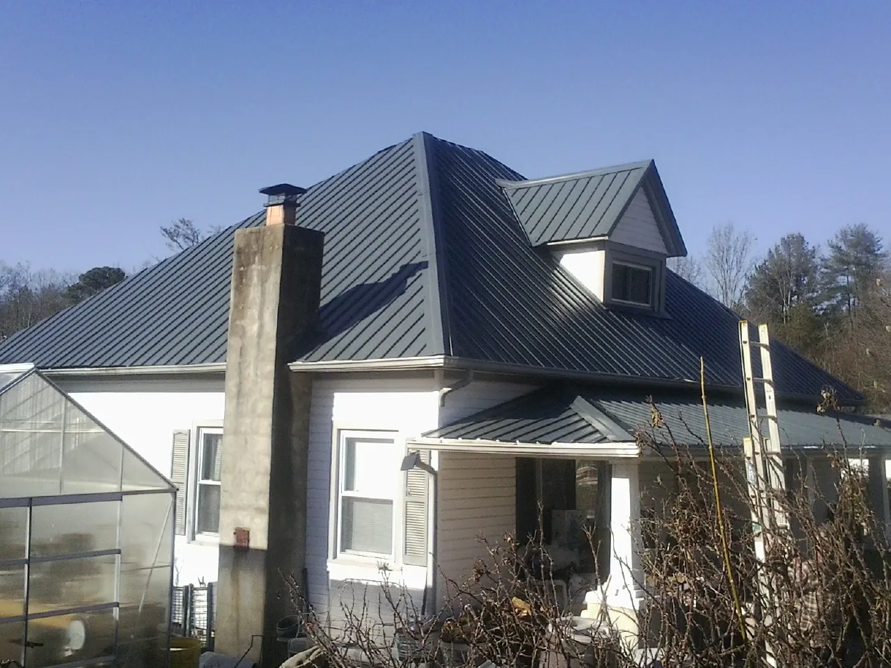 Dark blue standing seam metal roof on a white farmhouse with dormer — Slate & Tile Roof Repair by Roofing Brothers in Alcalde