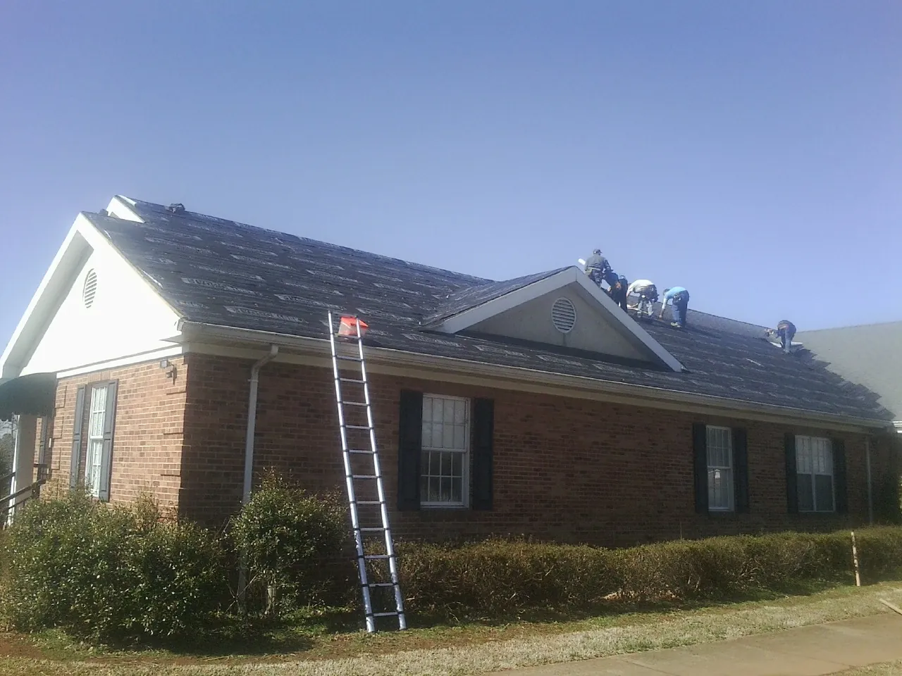 Crew tearing shingles off a brick ranch roof with a ladder set — Emergency Roof Repair work by our crew in Alcalde