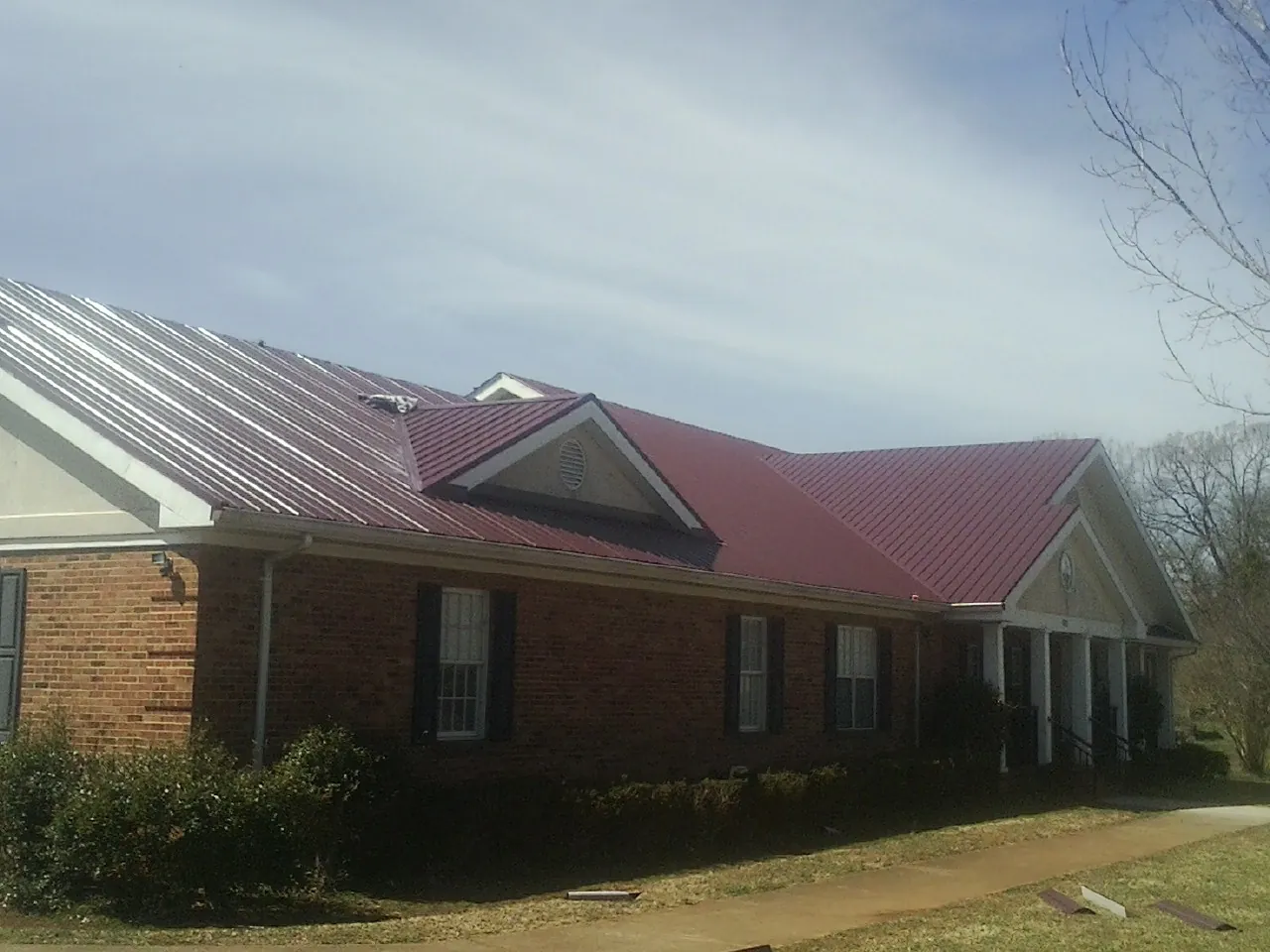 Red metal roof with gabled entries on a long brick building, from a Hail Damage Roof Repair job in Alcalde
