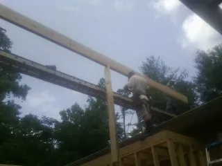 Carpenter setting a ridge beam over a new addition frame in Alcalde