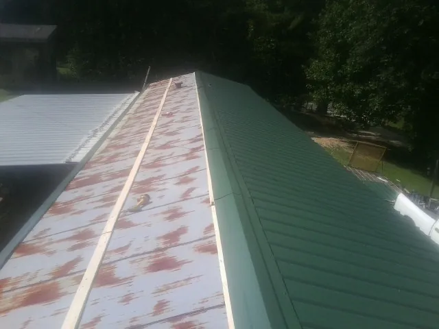 Old rusted panels beside newly installed green metal roofing — Wind Damage Roof Repair by Roofing Brothers in Alcalde
