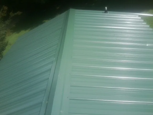 New green metal panels meeting at the ridge of a roof — Flat Roof Repair work by our crew in Alcalde