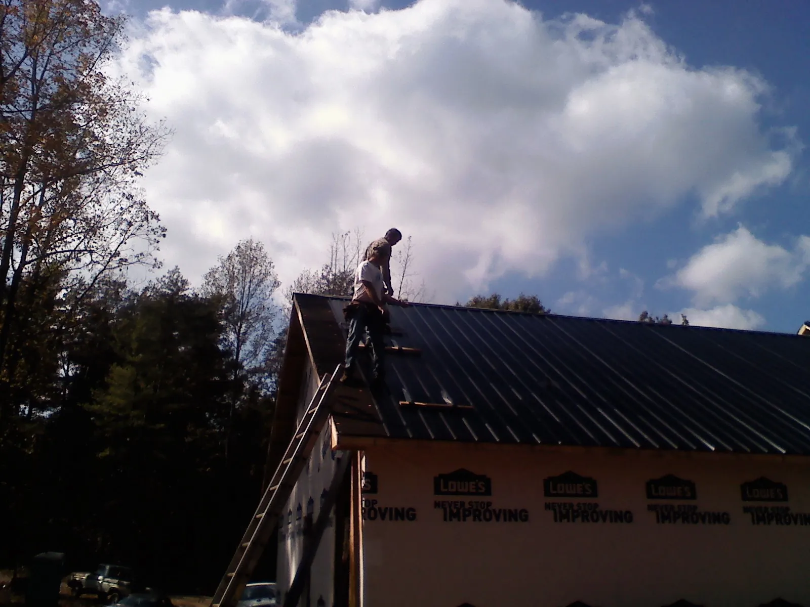 Roofer fastening dark metal panels high against a cloudy sky, from a Roof Inspection job in Alcalde