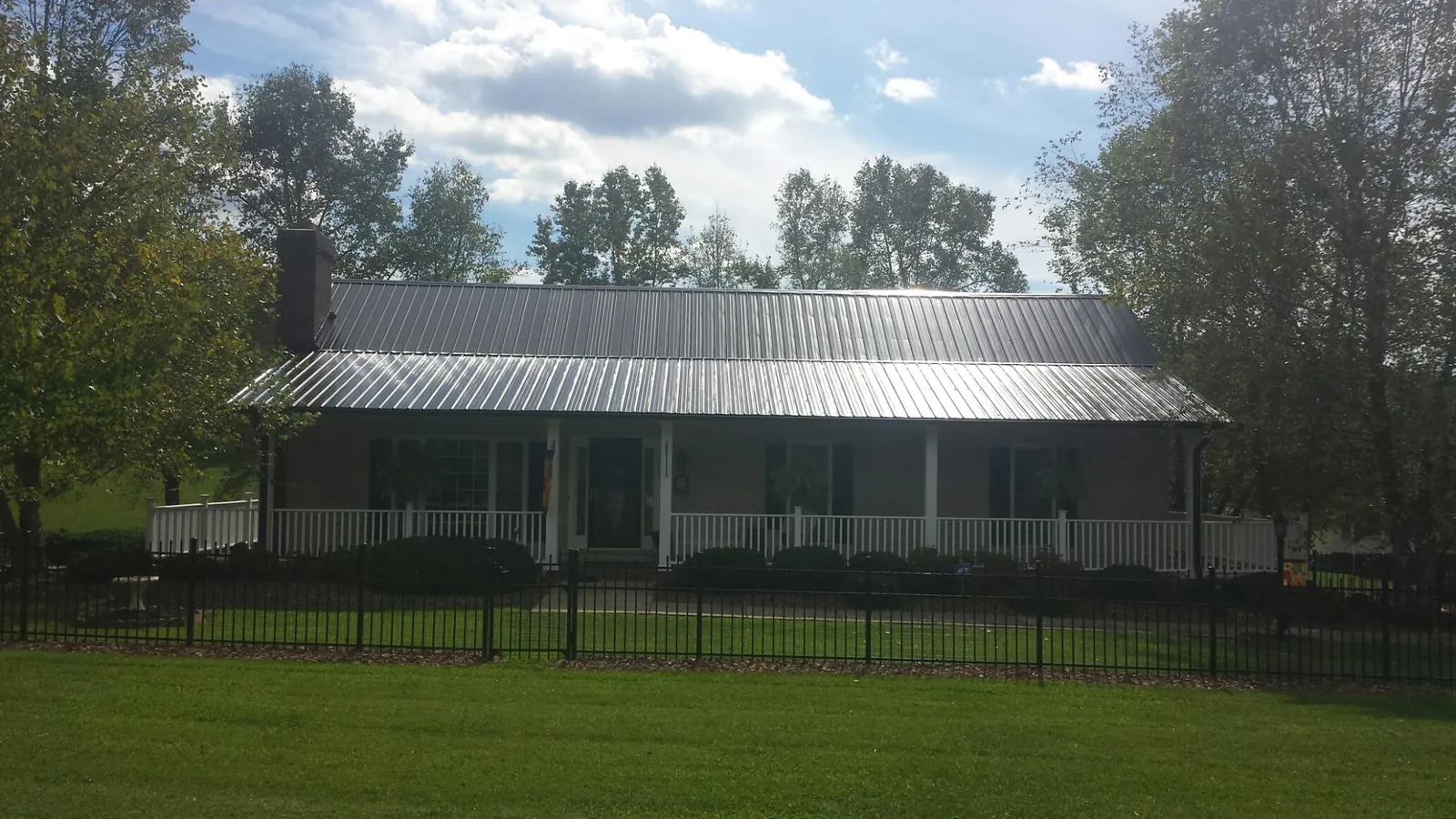 Gray metal roof on a brick ranch with a full width front porch — Gutter Guard Installation work by our crew in Alcalde