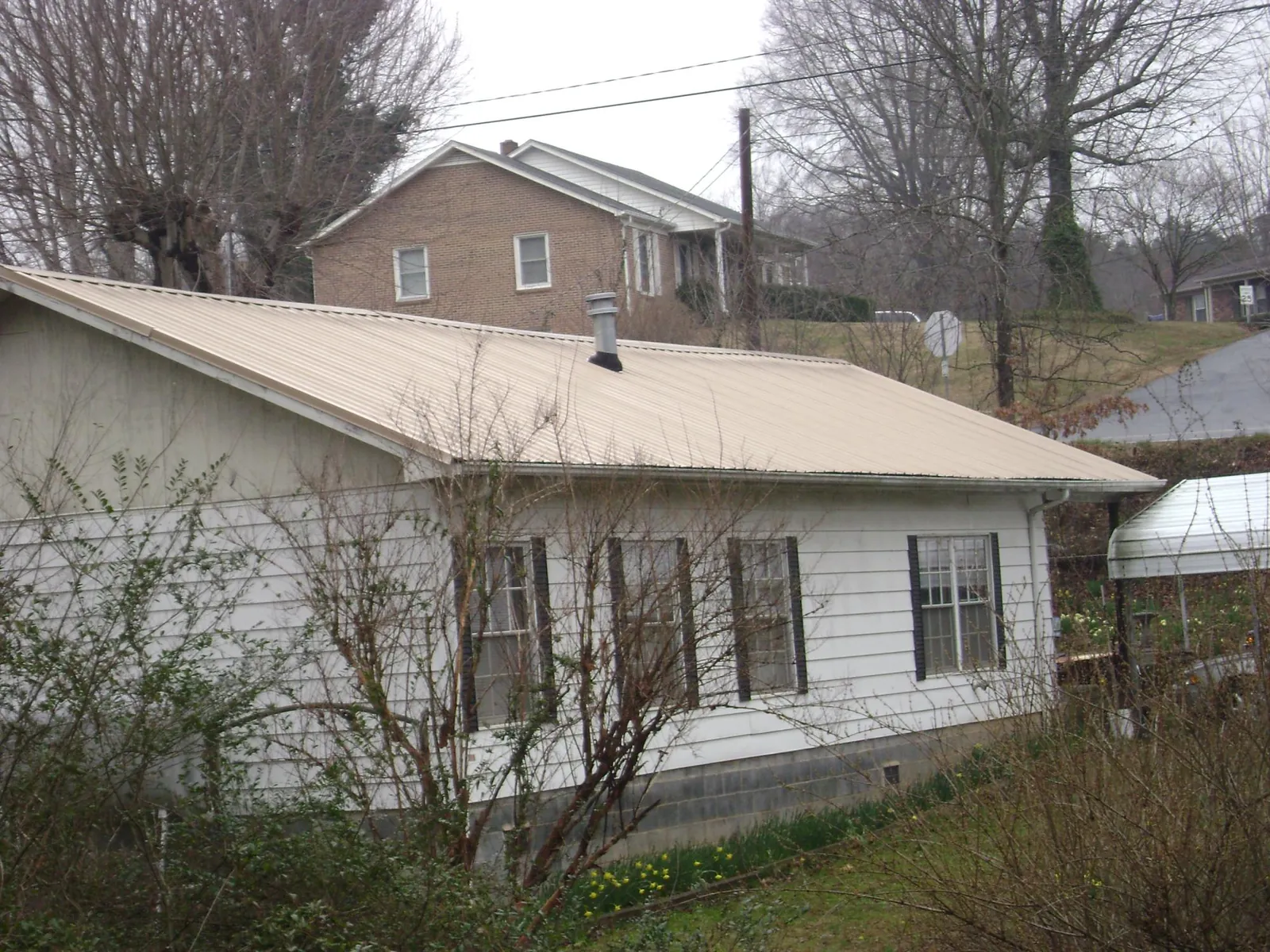 Tan metal roof on a white sided house set into a hillside — Commercial Roofing by Roofing Brothers in Alcalde