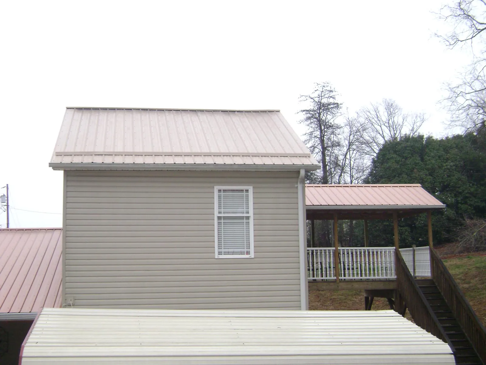 Tan metal roofs on a two story addition and attached porch, from a Roof Replacement job in Alcalde