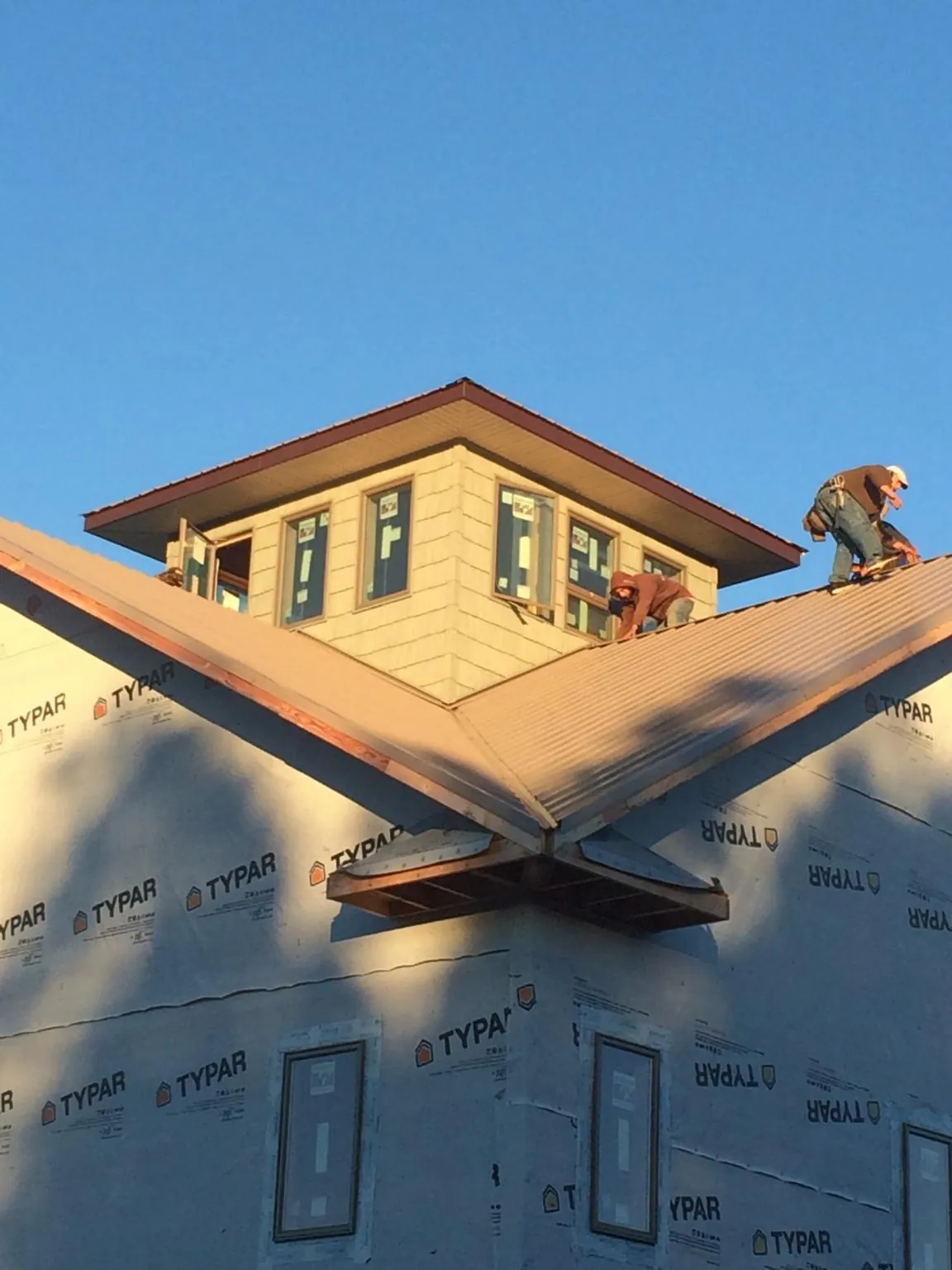 Roofers working around a rooftop cupola on a new metal roof at sunset — Roof Waterproofing in Alcalde by Roofing Brothers